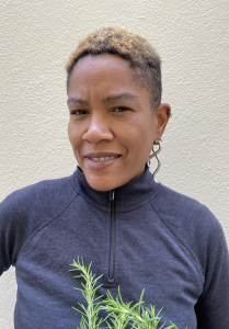 Photo of Kinshasa Bennett, in a blue zip up sweater against a beige background