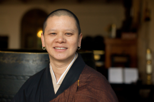 Photo of Rev. Lien, a short-haired Vietnamese person, smiling and wearing brown robes